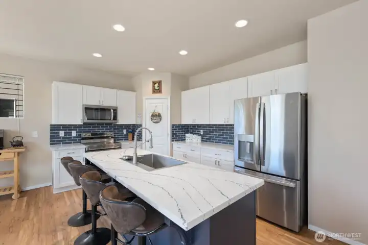 Open kitchen featuring white cabinetry, subway tile backsplash, stainless steel range, and large center island.