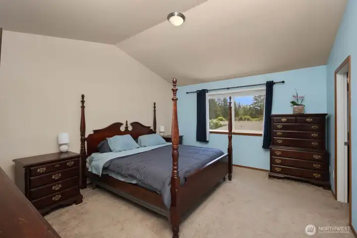 Spacious primary bedroom with vaulted ceilings, large window, and soft natural light.