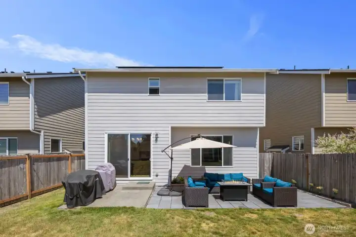 Rear exterior view featuring sliding glass door access, patio seating area, and fenced yard.