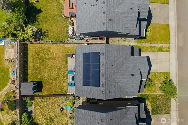 Aerial view showcasing the fully fenced backyard, patio space, storage shed, and solar panels.
