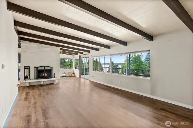 Large bright open living room with exposed wood beams and wood burning fireplace with stunning view of Dyes Inlet.