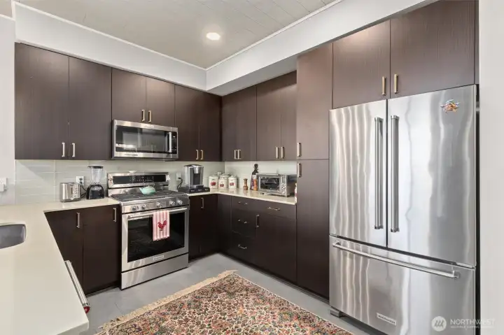 Gorgeous kitchen with modern finishes, 6-burner gas stove, glass tile backsplash, quartz countertops and eating bar. Notice the custom accent tile on the end of the countertop and the ceilings!