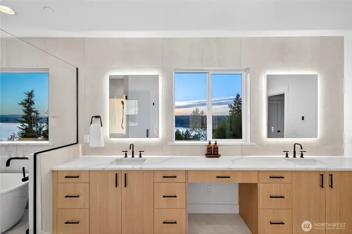 Primary ensuite with two vanity sinks, each with its own lighted mirror, and a shared window framing majestic Lake Sammamish views.