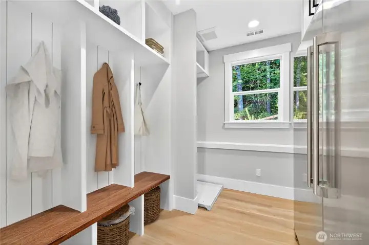 Mudroom off the garage features coat racks, a bench with under-seat storage, washer/dryer hookups, and a large high-end fridge. A bright window brings in natural light while maintaining privacy, and a cozy corner nook could serve as a pet area. Let you imagination run wild!