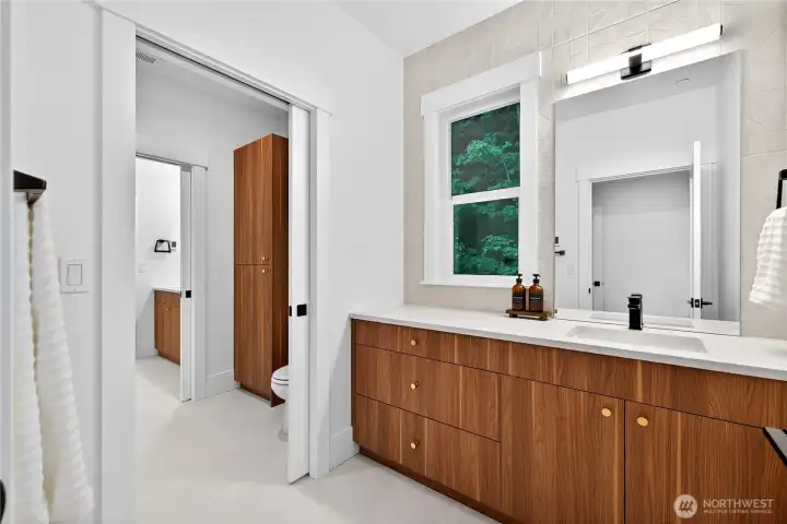 Jack-and-Jill bathroom connects the two upstairs secondary bedrooms, featuring a shared center area with a tub/shower combo and toilet, separated by locking pocket doors for privacy. Each bedroom has its own vanity area, and the bathroom includes heated floors.