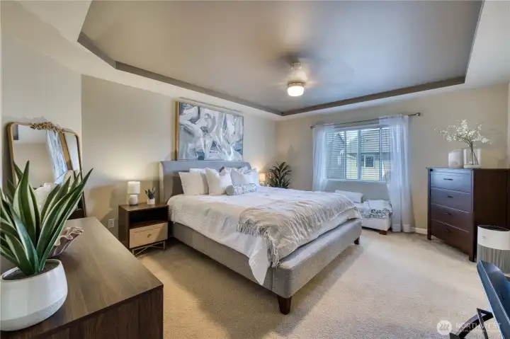 Primary suite is a spacious retreat with tray ceilings, ceiling fan and good natural light.