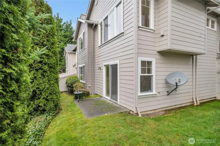 Back exterior with patio and lush backdrop.
