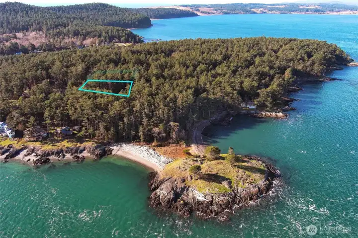 This aerial perspective shows the lot’s peaceful wooded setting near protected waters, rocky shoreline, and Cape San Juan community amenities.