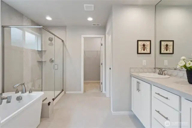 Wind down after a long day in this indulgent spa-inspired primary bathroom featuring a freestanding tub, oversized shower with ceramic tiled surround, dual vanity sinks, walk-in closet, enclosed water closet and tiled flooring.