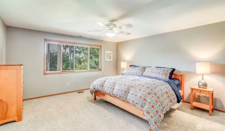 Generous primary bedroom space with large window framing beautifully curated backyard.