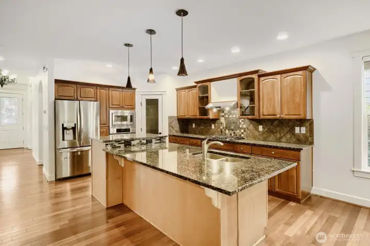 A center island with eating bar, granite countertops, stainless steel appliances, abundant cabinetry and counter space, and a pantry for additional storage complements this kitchen.