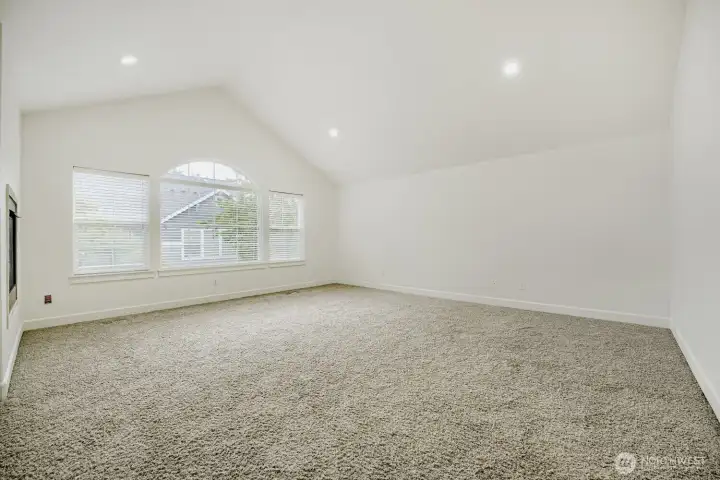 Luxury primary bedroom with a custom window, vaulted ceilings, and a see-through fireplace.