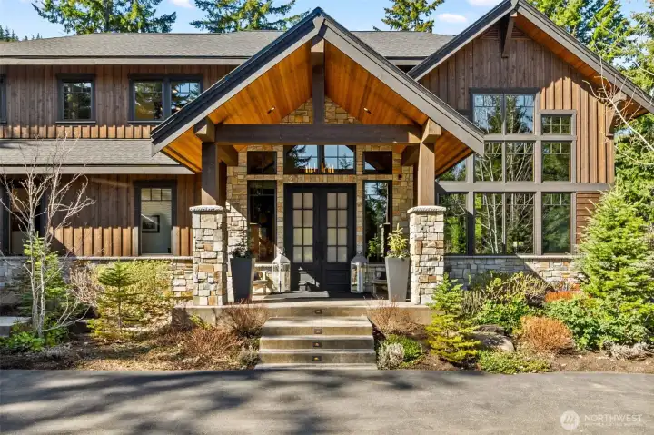 A grand yet welcoming entrance sets the tone with custom stonework and rich stained siding frame the covered porch, while expansive windows draw natural light into the home. A grand yet welcoming entrance sets the tone with custom stonework and rich stained siding frame the covered porch, while expansive windows draw natural light into the home.