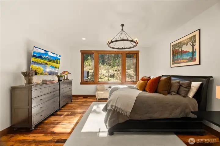Retreat to the spacious main floor primary suite, featuring a double-door entry, large windows with a private ridgeline view, and a comfortable seating area. Retreat to the spacious main floor primary suite, featuring a double-door entry, large windows with a private ridgeline view, and a comfortable seating area.