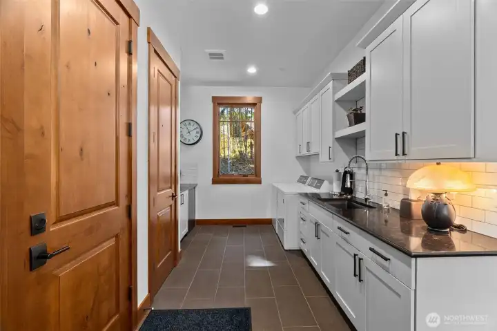 Thoughtfully designed, the main floor laundry room offers a work desk, bench, sink, and ample storage with cabinetry, countertops, and backsplash that seamlessly match the kitchen, plus convenient access to both the garage and driveway. Thoughtfully designed, the main floor laundry room offers a work desk, bench, sink, and ample storage with cabinetry, countertops, and backsplash that seamlessly match the kitchen, plus convenient access to both the garage and driveway.