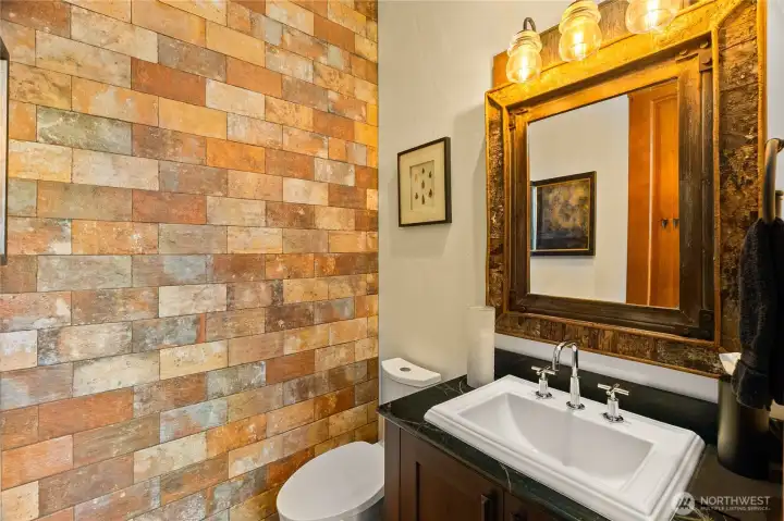The main floor powder room charms with a soapstone countertop, unique glass electric line insulator wall-mounted downlight and a faux brick wall feature. All toilet seats throughout the home are heated for an extra touch of luxury. The main floor powder room charms with a soapstone countertop, unique glass electric line insulator wall-mounted downlight and a faux brick wall feature. All toilet seats throughout the home are heated for an extra touch of luxury.
