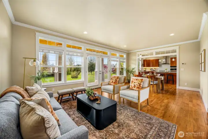 Open concept living room, connected to dining and kitchen, filled with natural light from panoramic windows and French doors that create a bright, open feel.