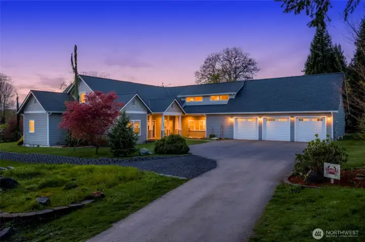 Twilight view of the front view of house with three car garage, RV gravel parking pad & landscaping.