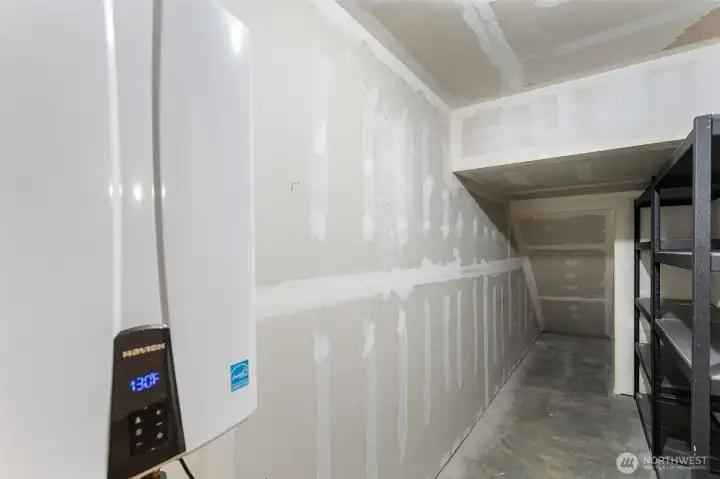 Storage space within garage area with shelving and a newer Navien tankless hot water heater.