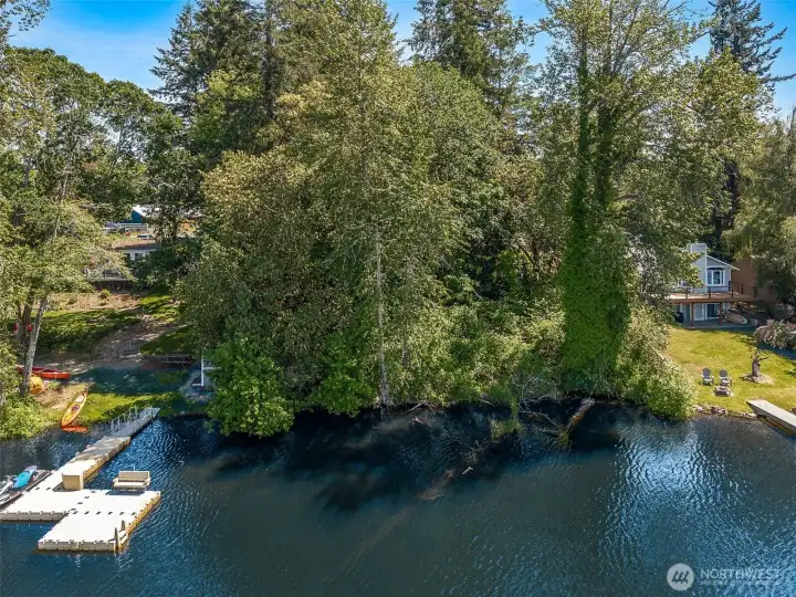 From directly above the lake, you can really appreciate just how rare this opportunity actually is. One of the last remaining vacant waterfront parcels on Long Lake, this .5432-acre property delivers an exceptionally gentle slope toward 110 feet of shoreline, something that becomes harder and harder to find as more waterfront lots get built out over time. The surrounding neighboring homes beautifully demonstrate the versatility of the terrain too. Some owners have embraced terraced landscaping and elevated outdoor living spaces to maximize sweeping lake views, while others have opted for softer rolling lawns flowing directly into the water. This parcel gives you the freedom to decide your own version of lakefront living instead of inheriting somebody else’s choices. And somehow it still manages to feel worlds away while remaining incredibly accessible at roughly one hour from Seattle and two hours from Portland. Build the dream house. Build the “we should have done this years ago” prop