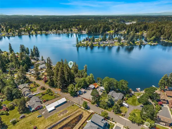 This closer shot of the lot really lets the personality start shining through. The street side is lined with tall mature evergreens creating that immediate Pacific Northwest “private forest retreat” feeling, while the vegetation gradually transitions into more deciduous trees as you move closer toward the waterfront, allowing more seasonal light and openness near the lake. It creates such a naturally layered setting for future home design because you can preserve privacy where you want it while selectively opening lake views exactly how you envision them. You can also see the surrounding waterfront homes tucked throughout the shoreline, many clearly showing strong pride of ownership and beautifully maintained properties that help reinforce the overall quality and appeal of this Long Lake neighborhood. And way off in the far southeast distance, yes, that is Mount Rainier peeking out in the corner!