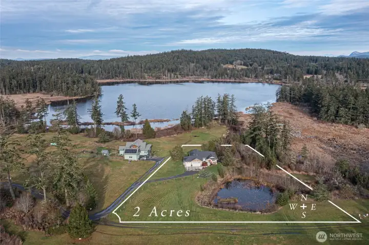 A stunning aerial view highlights the private 2-acre property, complete with a pond, manicured lawn, and wooded backdrop leading to the shoreline.