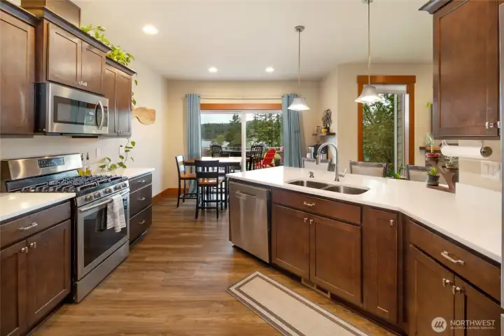 Modern kitchen featuring stainless steel appliances, quartz countertops, rich wood cabinetry, and a walk-in pantry.