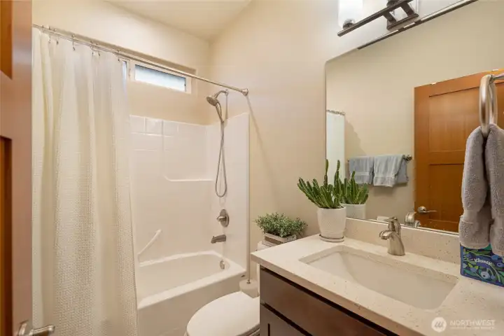 Bright full bathroom with modern finishes, quartz vanity, and a shower/tub combo for convenience.