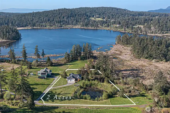 A stunning aerial view highlights the private 2-acre property, complete with a pond, manicured lawn, and wooded backdrop leading to the shoreline.