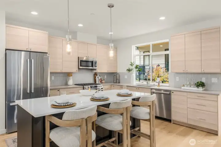 Chef’s kitchen with quartz countertops, premium stainless steel appliances, and a generous breakfast bar. (photos of model home)