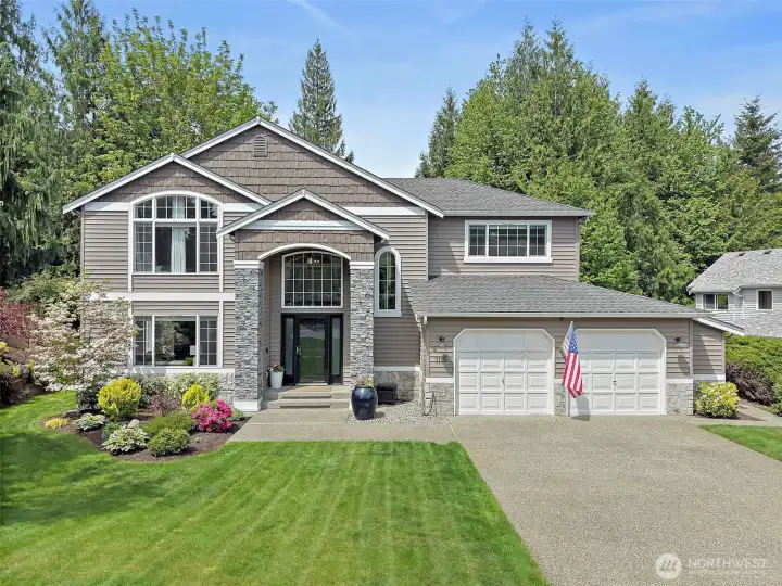 North Bend two-story home exterior with faux stone-accented entry, large front windows, attached 2-car garage, landscaped yard, and mature greenery.