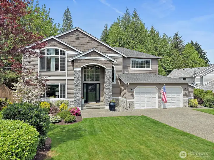 North Bend two-story home exterior with faux stone-accented entry, large front windows, attached 2-car garage, landscaped yard, and mature greenery.