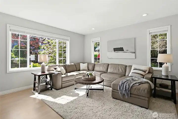 Living room with large front windows, abundant natural light, neutral wall color, recessed lighting, barn door, and spacious seating area.