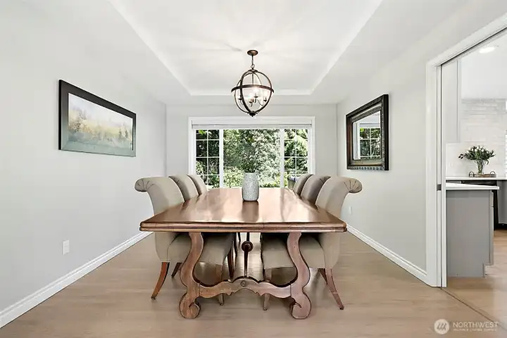 Dining room with large backyard-facing window, tray ceiling, statement light fixture, neutral finishes, and easy flow to nearby living spaces.