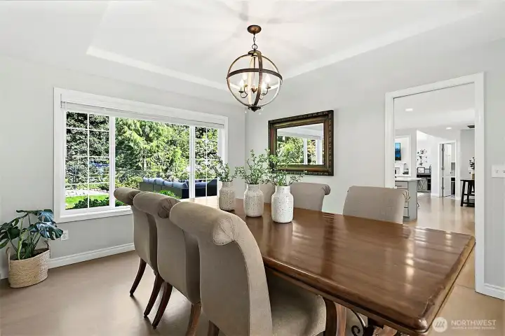 Dining room with large backyard-facing window, tray ceiling, statement light fixture, neutral finishes, and easy flow to nearby living spaces.
