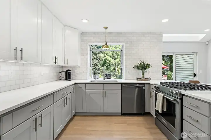 Chef’s kitchen with quartz countertops, subway tile backsplash, two-tone shaker cabinets, stainless appliances, recessed lighting, and backyard views.