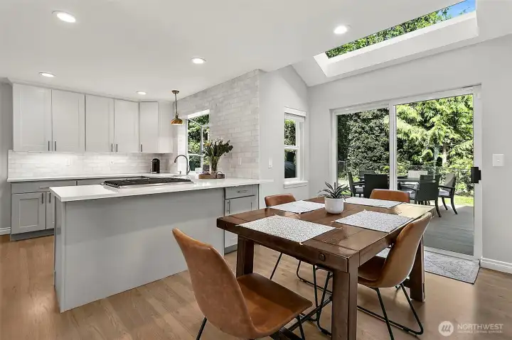Breakfast dining area with skylight, hardwood flooring, sliding door access to the new deck, backyard views, and open flow to nearby living spaces.