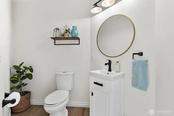 Half bathroom with pedestal-style vanity, round mirror, modern fixtures, neutral finishes, and wood-look flooring.