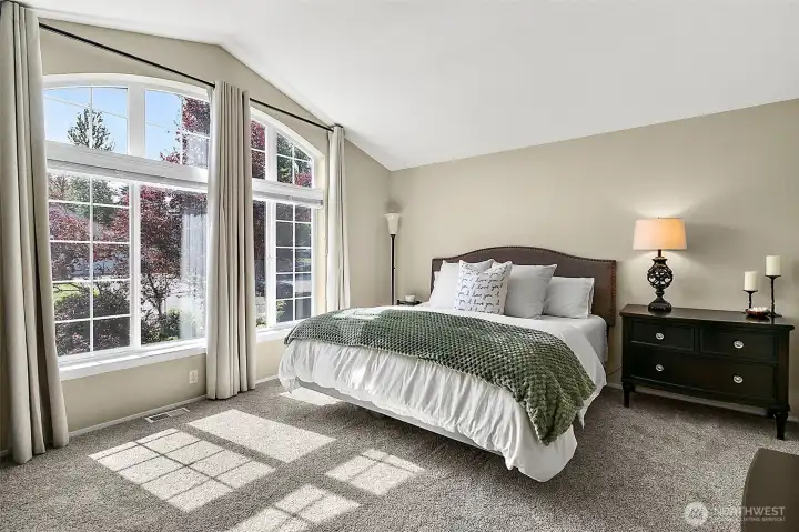 Primary bedroom with vaulted ceiling, arched windows, natural light, neutral finishes, carpet flooring, and spacious layout.