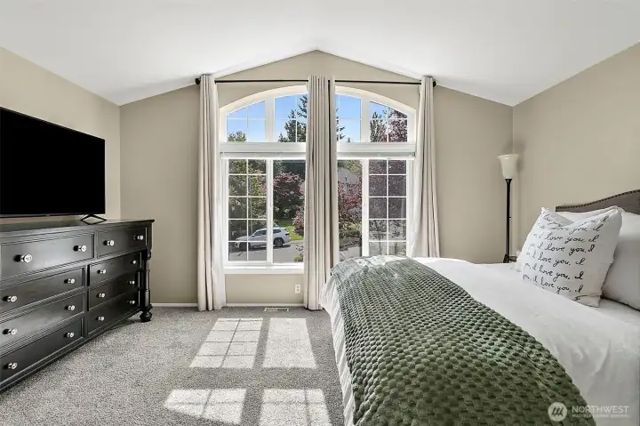 Primary bedroom with vaulted ceiling, arched windows, natural light, neutral finishes, carpet flooring, and spacious layout.