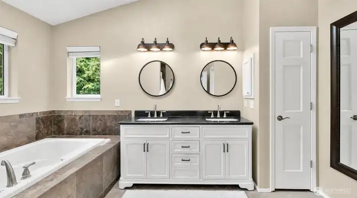 Primary 5 piece bathroom with skylight, soaking tub, walk-in tile shower, dual sink vanity, stone tile accents, and natural light.