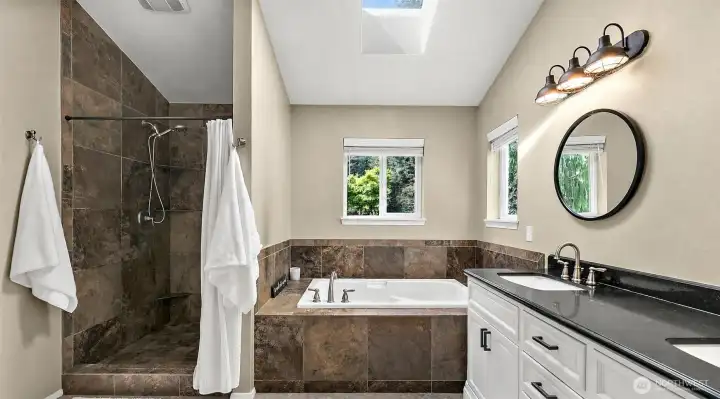 Primary 5 piece bathroom with skylight, soaking tub, walk-in tile shower, dual sink vanity, stone tile accents, and natural light.