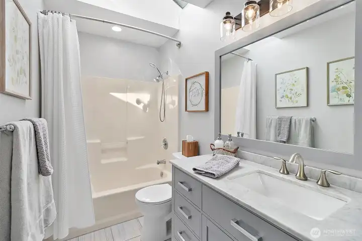 Full bathroom with skylight, updated vanity, tub and shower combo, modern lighting, neutral finishes, and bright tile flooring.
