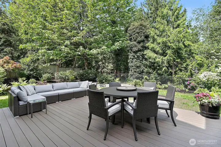 New deck with outdoor seating, dining space, sliding door access, fenced backyard, mature landscaping, and hillside views.