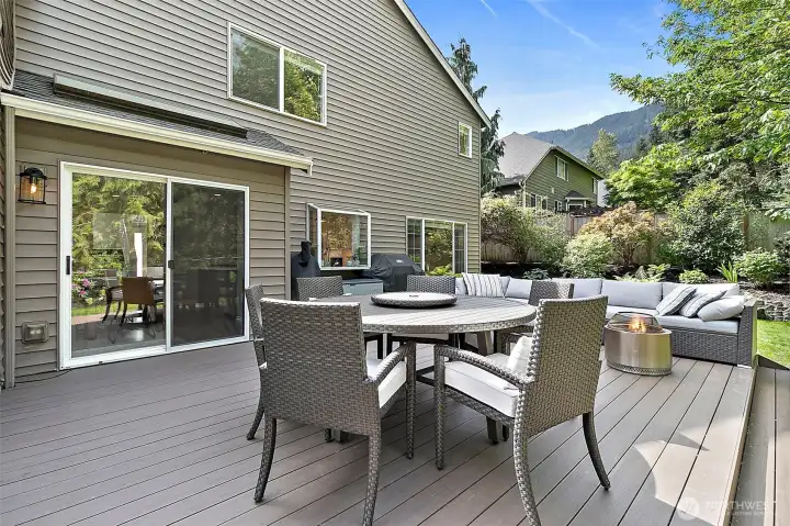 New deck with outdoor seating, dining space, sliding door access, fenced backyard, mature landscaping, and hillside views.