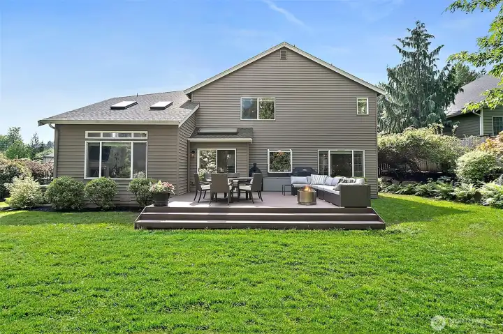 New deck with outdoor seating, dining space, sliding door access, fenced backyard, mature landscaping, and hillside views.