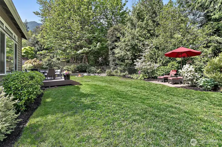 Fully fenced backyard with new deck, outdoor seating areas, mature landscaping,  and greenbelt backdrop.