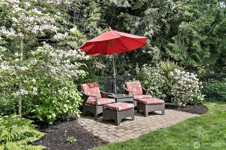Fully fenced backyard with new deck, outdoor seating areas, mature landscaping,  and greenbelt backdrop.