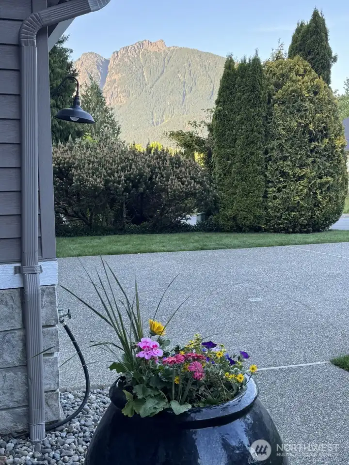 Front entry view with landscaped planter, driveway, mature greenery, and scenic mountain backdrop.