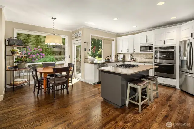Wide angle photo of kitchen and eating area shows off the beautiful hardwood floors, ample kitchen space and updated, stainless appliances.